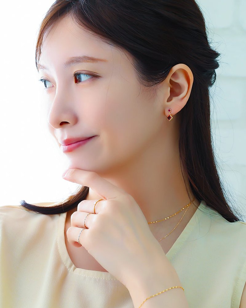 アイボリーのトップスに、イエローゴールドのガーネットのピアスとリングを合わせた女性