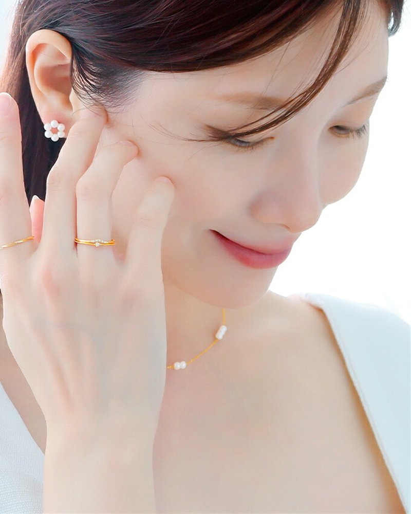 頬に手を添え、イエローゴールドの細いリングとパールのピアスを合わせた女性