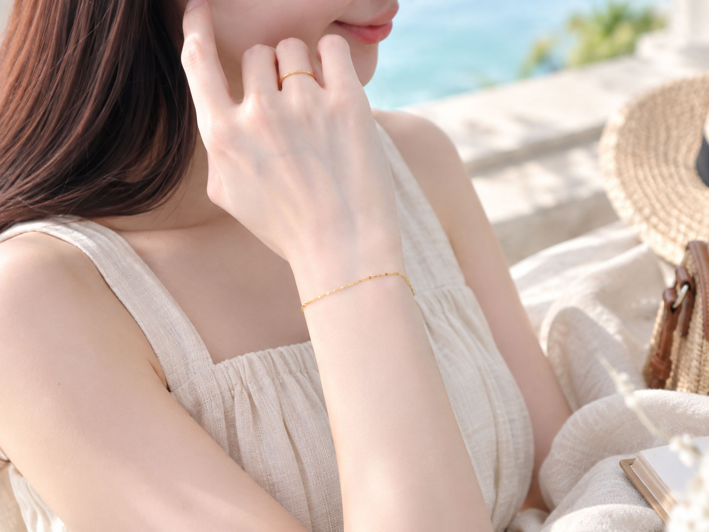 海辺のテラスで、リネンのワンピースに細いゴールドのブレスレット