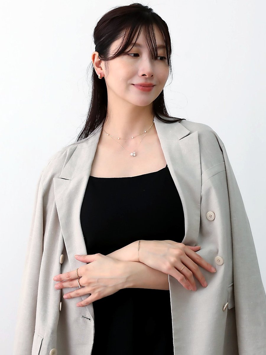 黒のワンピースにベージュのジャケットを肩掛けし、パールのネックレスを重ねた女性