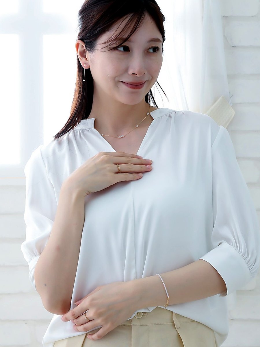 白いブラウスに、パールのステーションネックレスと揺れるピアス、細いリングを合わせた女性